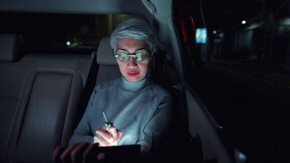 老年妇女在城市灯光下在车里使用智能手机