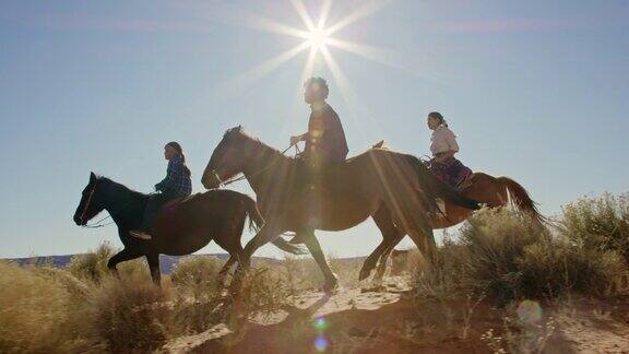 几个年轻的印第安人(纳瓦霍)孩子骑着马穿过纪念碑谷沙漠和他们的宠物狗在亚利桑那州犹他州在一个晴朗明亮的日子