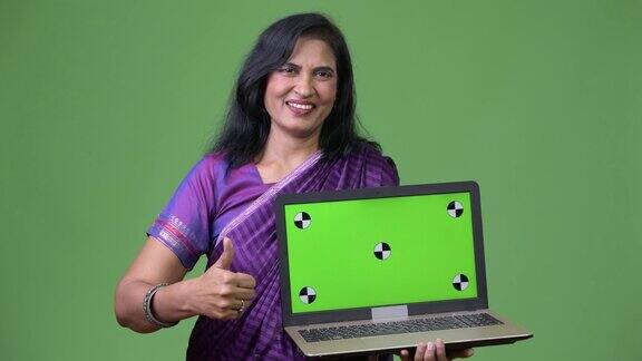 成熟快乐美丽的印度女人展示笔记本电脑并竖起大拇指