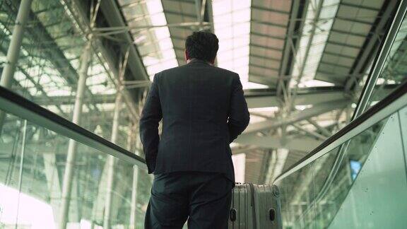 商人站在机场自动扶梯上的后视图