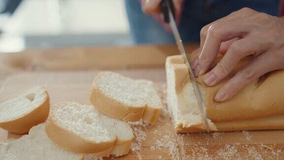 年轻的亚洲女厨师双手握着刀在厨房桌子上的木板上切着全麦面包