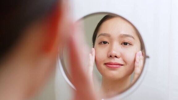 年轻的亚洲美女应用精华液和保湿面霜在健康的面部皮肤和看镜子亚洲美容皮肤