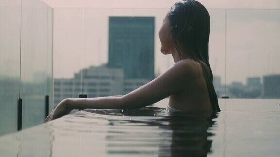 放松的年轻女子游泳在酒店的游泳池在日落