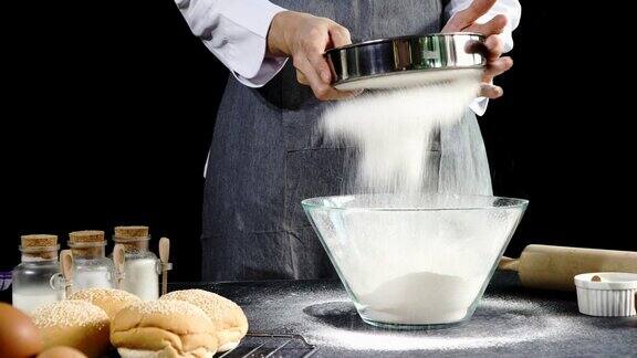 自制烘焙食品概念身穿灰色围裙的年轻面包师将面粉筛入玻璃碗中揉面前准备面团