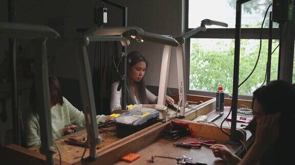 亚裔华裔女大学生在工作台上并排制作珠宝设计