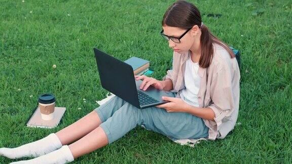 十几岁的女学生坐在户外读书看她的书平板电脑和笔记本回到学校在校园里或公园里女学生躺在草地上使用笔记本电脑远程学习
