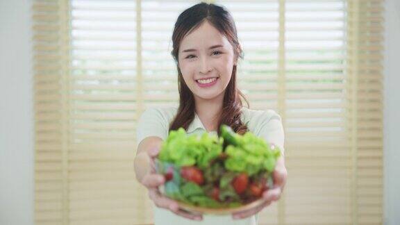 一个微笑的女人在家里的厨房里吃着新鲜的沙拉素食