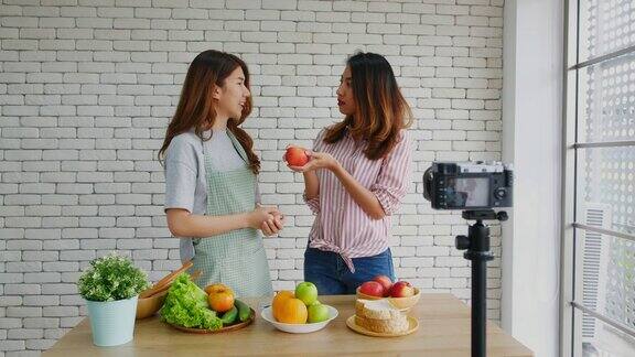 两个年轻的亚洲女性美食博主拿着红苹果一边讲解健康的食物和健康的生活方式一边录制视频播放Vlog健康的生活方式