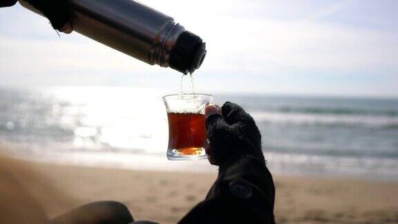 冬天在海滩上一名妇女正在把热水瓶里的茶倒进马克杯里