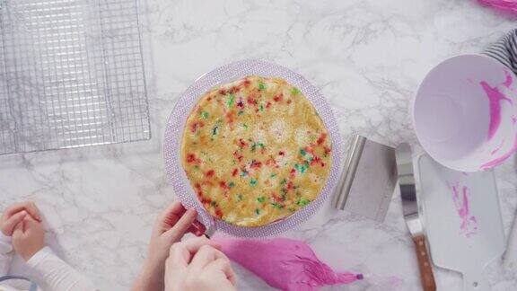 用粉色奶油糖霜给圆形的funfetti蛋糕层上糖霜