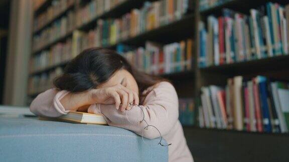 疲惫的戴眼镜的亚洲女学生睡在图书馆的书上