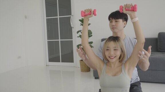 男教练正在教亚洲女子举哑铃他们在家锻炼的方式