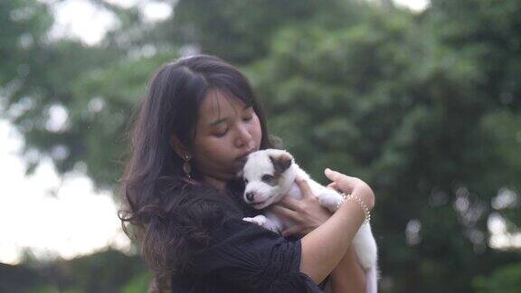 年轻女子抱着和抚摸一个可爱的小狗在草坪上的自然