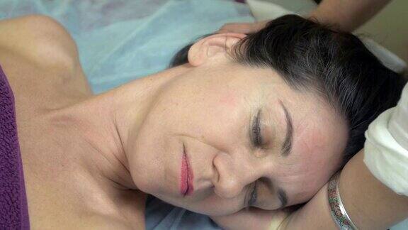 女按摩师在专业沙龙为年轻女性做头部治疗按摩