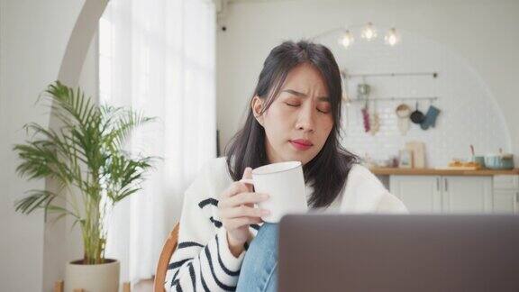 自由亚洲女士休闲服装使用笔记本电脑和喝咖啡在家里的厨房在家工作、远程工作、远程教育、保持社交距离、隔离预防冠状病毒