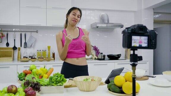 年轻的亚洲运动女性食品博主说话同时录制视频准备绿色沙拉在厨房教程视频到社交网络通过互联网在家概念