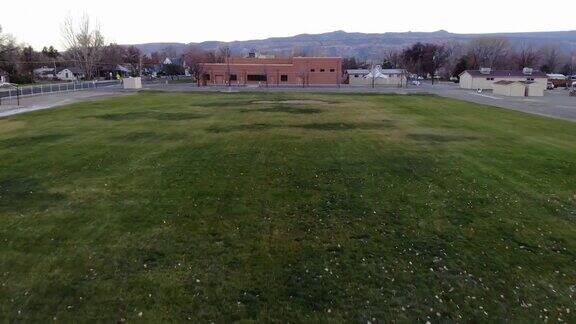 无人机拍摄的镜头穿过学校建筑后面的运动场的球门柱后面背景是群山