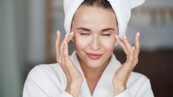 肖像妇女在浴衣与毛巾在头上应用霜在她的脸上