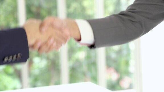 两个商人近距离站起来在会议室里互相握手处理商务协议