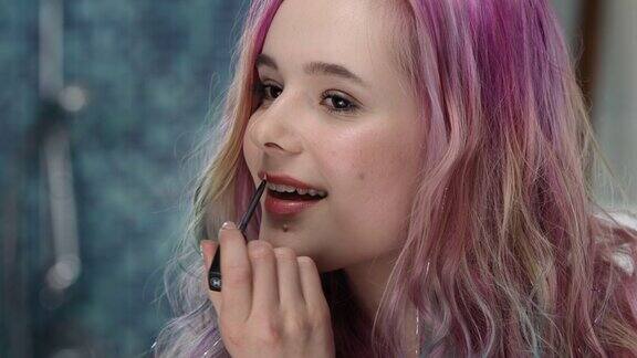 一位粉色头发的青春期少女正在尝试在嘴唇上涂唇彩