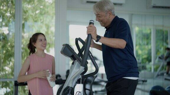 在繁忙的健身房里一位年轻的亚洲女性微笑着帮助一位年长的客户