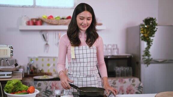 年轻漂亮的亚洲女人穿着围裙在厨房的煎锅上撒上黑胡椒粉煮牛排