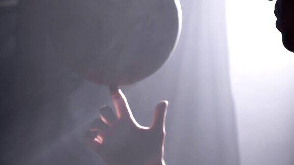 篮球运动员在黑暗的、雾蒙蒙的房间里用一根手指旋转着球