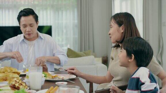 幸福的亚洲家庭聪明的父亲美丽的母亲和6岁的儿子一起吃早餐然后送小儿子去上学年轻的父亲正在喂他的儿子吃饭与家人共度时光
