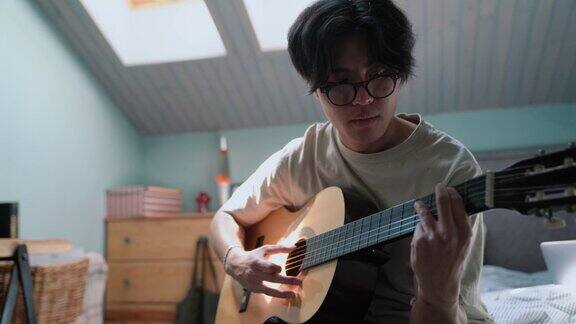 漂亮的亚洲男人在床上弹吉他