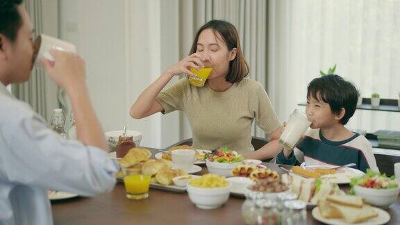 花时间在一起亚洲家庭年轻英俊的父亲和6岁的儿子喝一杯牛奶美丽的母亲喝橙汁在一起吃早餐在早上