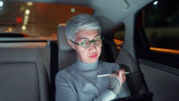老年妇女在城市灯光下在车里使用智能手机