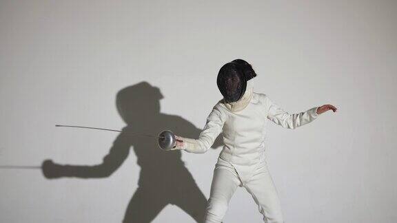 一名年轻女子击剑手的肖像戴上头盔投掷攻击的打击一名运动员在白色背景和阴影的黑暗工作室里摆姿势慢动作