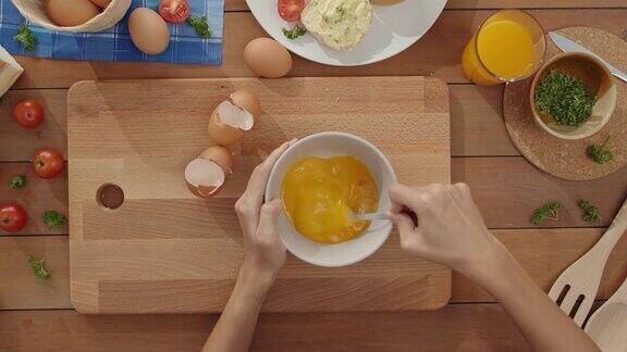 年轻的亚洲女厨师用手把鸡蛋打到陶瓷碗里在厨房桌子上的木板上用蔬菜做煎蛋卷