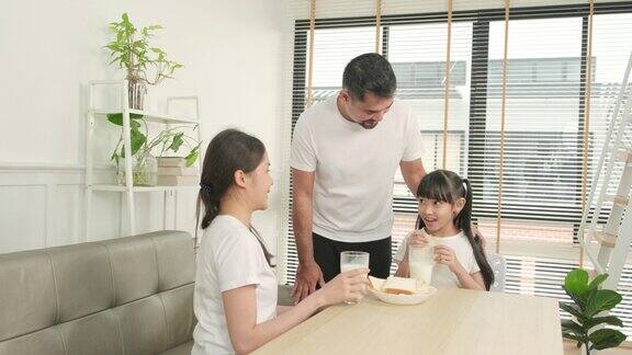 一个亚洲泰国家庭在一杯新鲜的白牛奶和面包一起欢乐