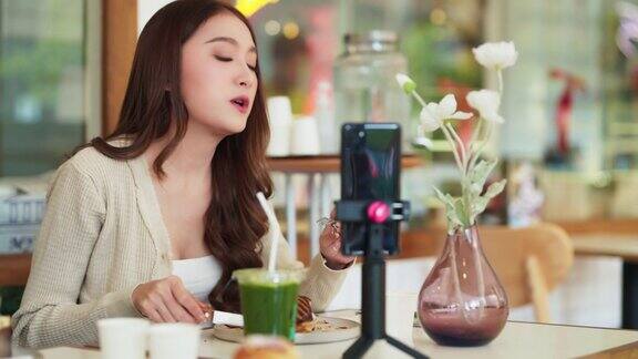 有吸引力的亚洲女性美食视频博主喜欢在咖啡馆餐厅吃甜食咖啡并在社交媒体上与粉丝分享他们的在线直播时间