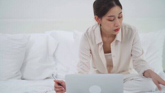 亚洲女商人使用科技平板电脑工作并在床上写笔记本