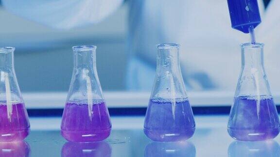 在化学实验室进行的变色液体的医学研究实验注射器将蓝色的碱性或酸性化学物质倒入一排锥形烧瓶以创造稳定的溶液的特写