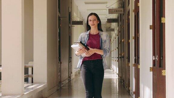 一个女大学生拿着课本走在教学楼的走廊上教育回归学校理念