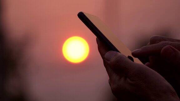 在太阳升起的背景下亚洲男子使用手机的特写