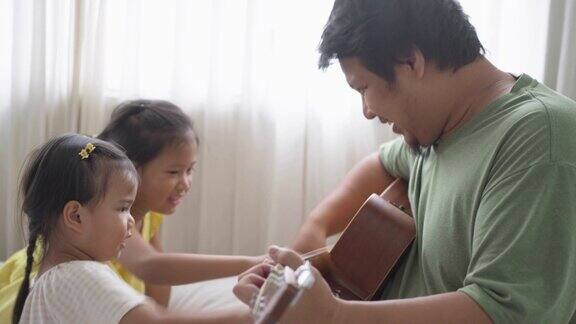 父亲和两个女儿在家里一起弹吉他