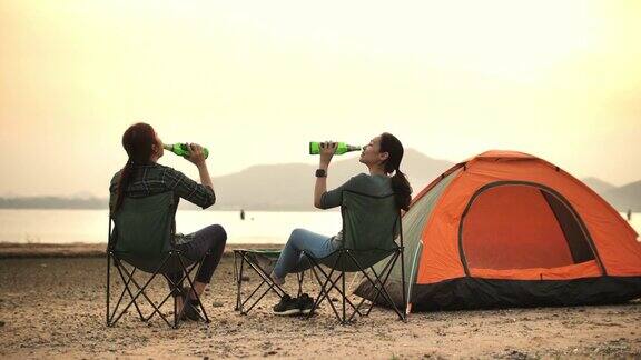 两个露营的女人喝着啤酒享受日落看着美丽的山