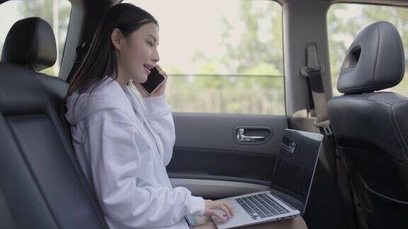 女商人在出租车上一边用笔记本电脑一边打电话坐在汽车后座上用笔记本电脑和手机的女人