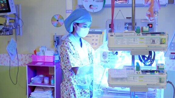 新生儿重症监护室的护士在检查一个在保温箱里接受黄疸治疗的可爱的小婴儿时正在讨论一个病例