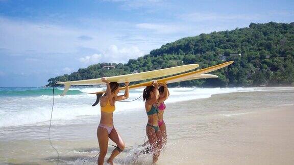在夏日阳光明媚的日子里一群亚洲妇女手持冲浪板从海洋中走出来