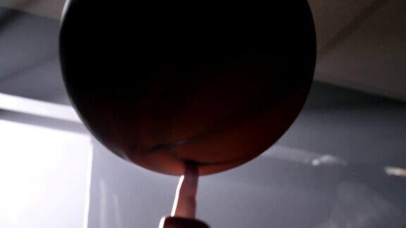 篮球运动员在他的手指上旋转球的近距离镜头黑暗的、雾蒙蒙的房间和泛光灯