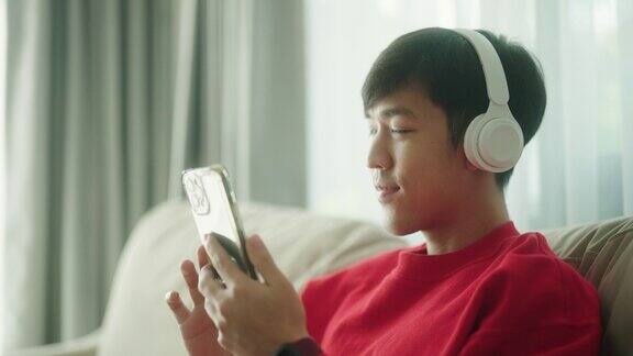 年轻的亚洲男子在家里的沙发上使用智能手机