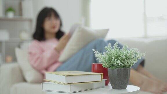 快乐快乐的亚洲女人微笑着坐在家里客厅的沙发上看书亚洲女人放松看书坐在家里的沙发上微笑在家活动爱好