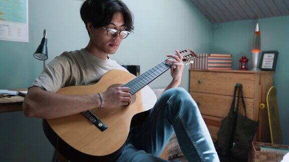 自信的亚洲男子在床上弹吉他