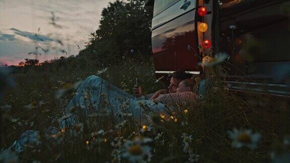 DS夫妇躺在露营车旁边的草地上玩智能手机