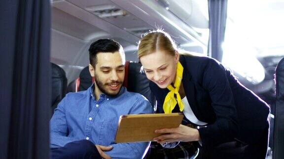 空姐向西班牙男性乘客展示带有菜单的平板电脑他们在机上商务舱的一个商业航空内部可见